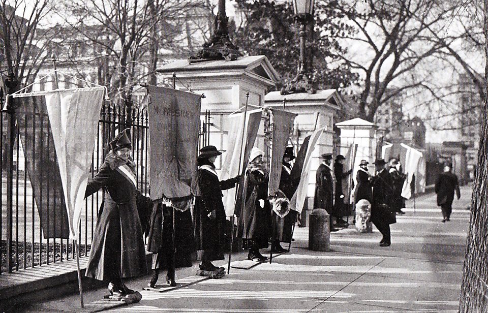 Image: black and white photo of suffragettes lined up in front of the White House