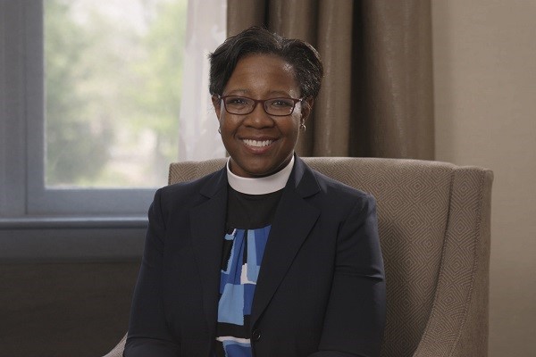 Reverend Jennifer Baskerville-Burrows, sitting in a chair, smiling at the camera