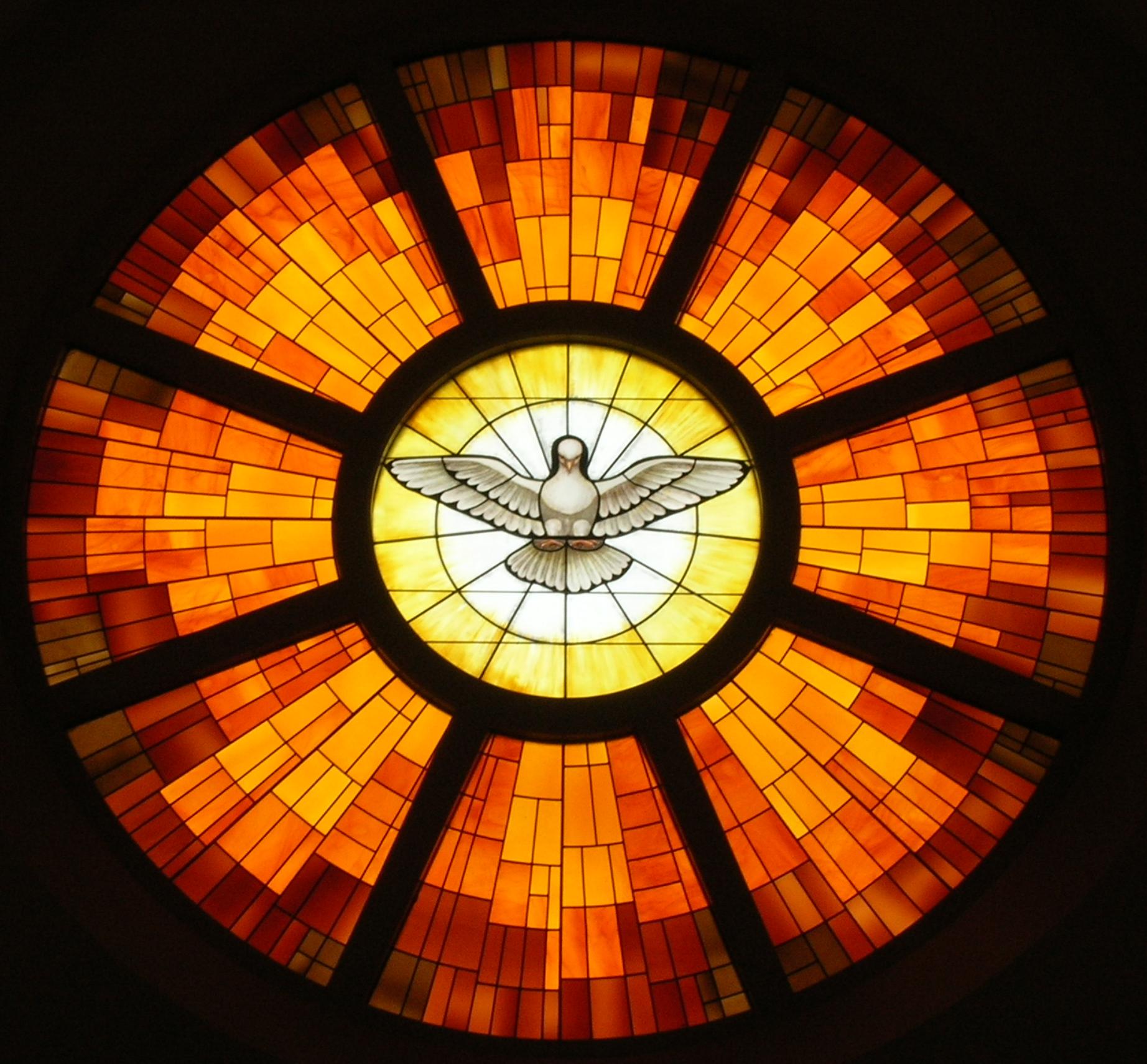 A picture of a stain glass window. It is a Christian Pentecost symbol, with a dove at the center, surrounded by flame.