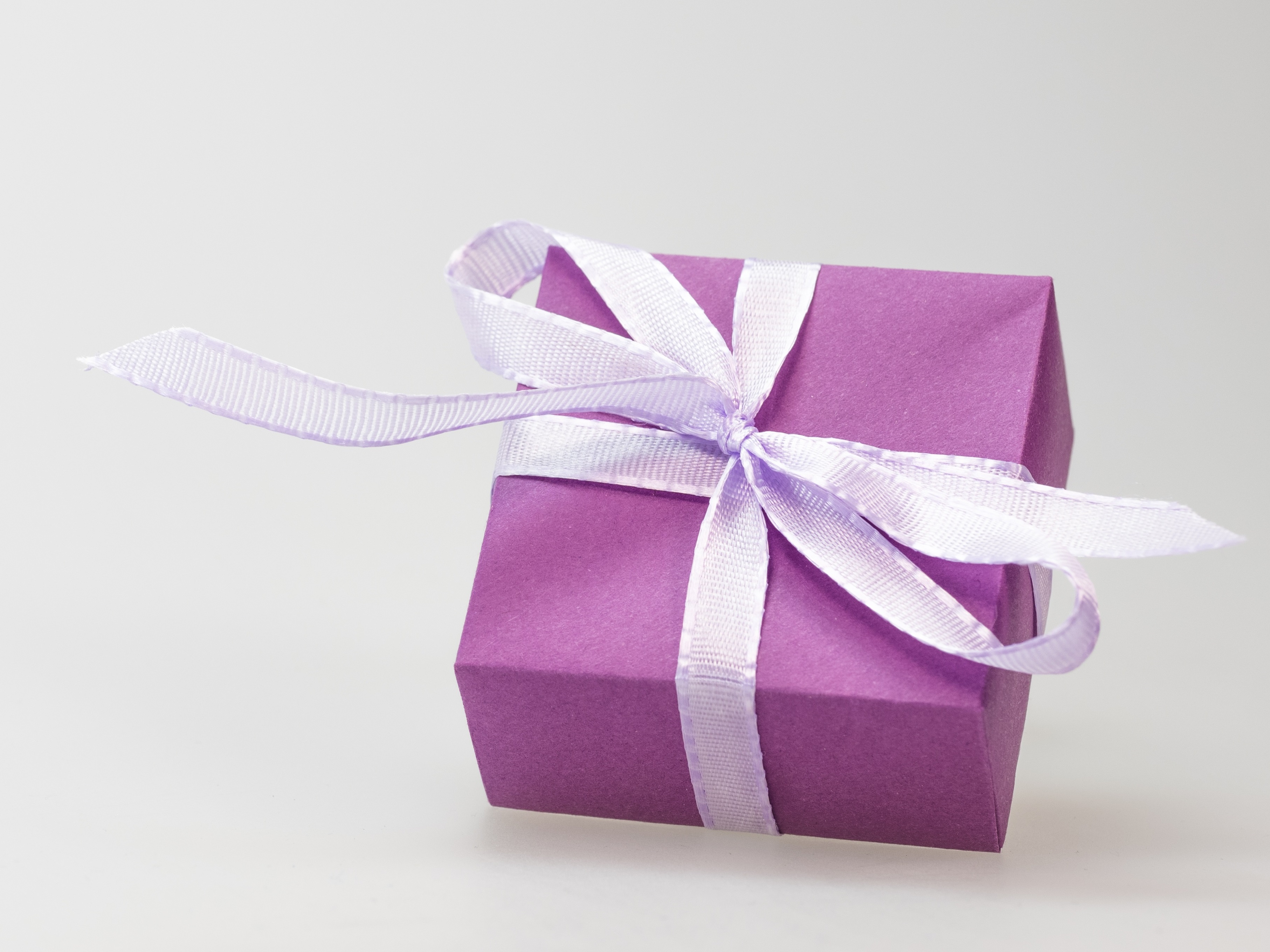 A picture of a present wrapped in solid purple paper and tied in a white ribbon.